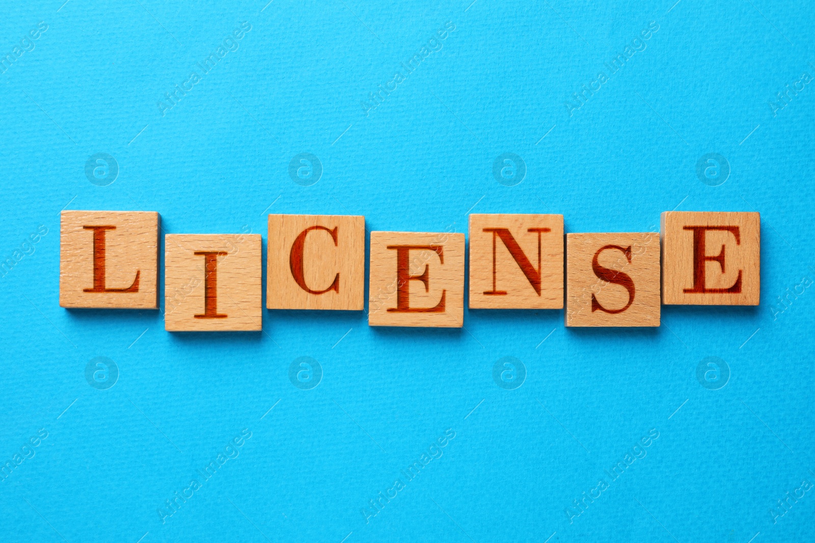 Image of License word made of wooden squares with letters on light blue background, top view