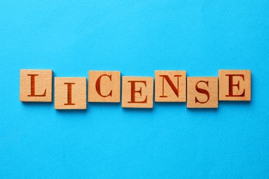 Image of License word made of wooden squares with letters on light blue background, top view