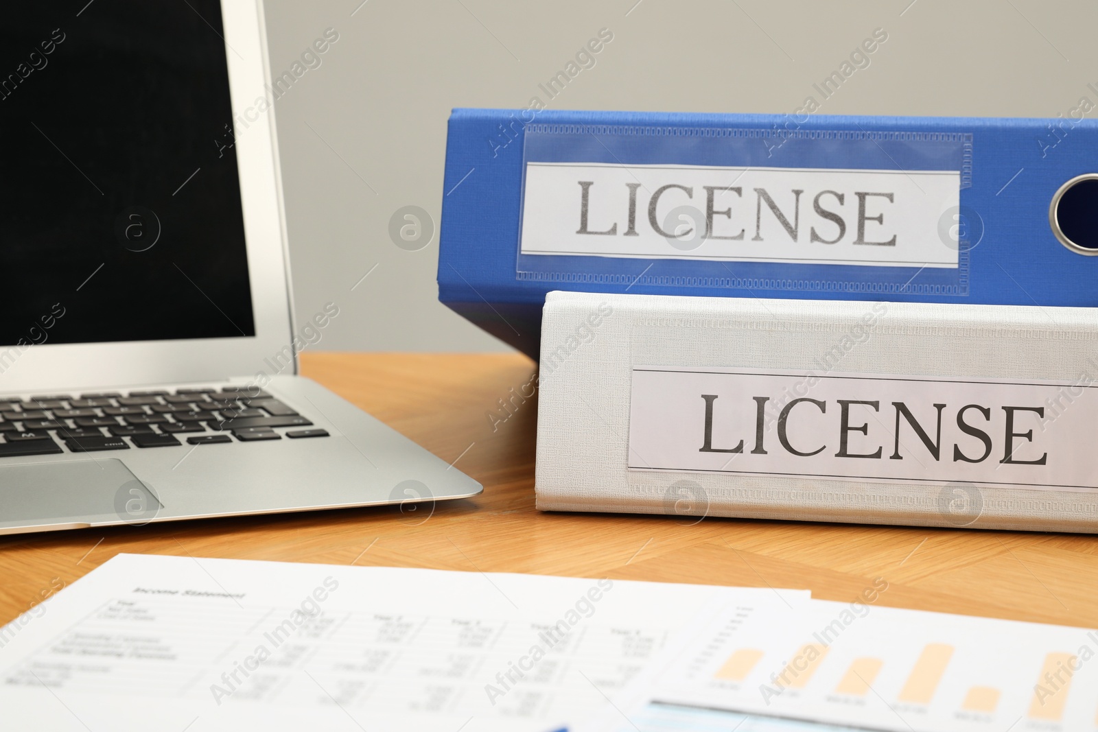 Image of File folders with labels License and laptop on wooden table, closeup