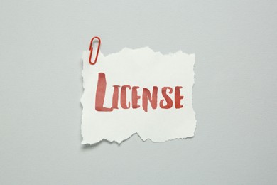 Image of Piece of paper with word License and paperclip on white background, top view