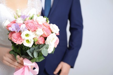 Photo of Bride with beautiful wedding bouquet and groom on light background, closeup. Space for text