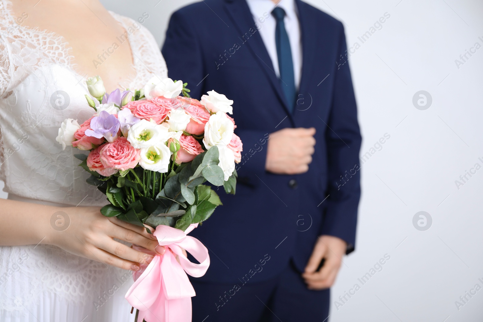 Photo of Bride with beautiful wedding bouquet and groom on light background, closeup. Space for text