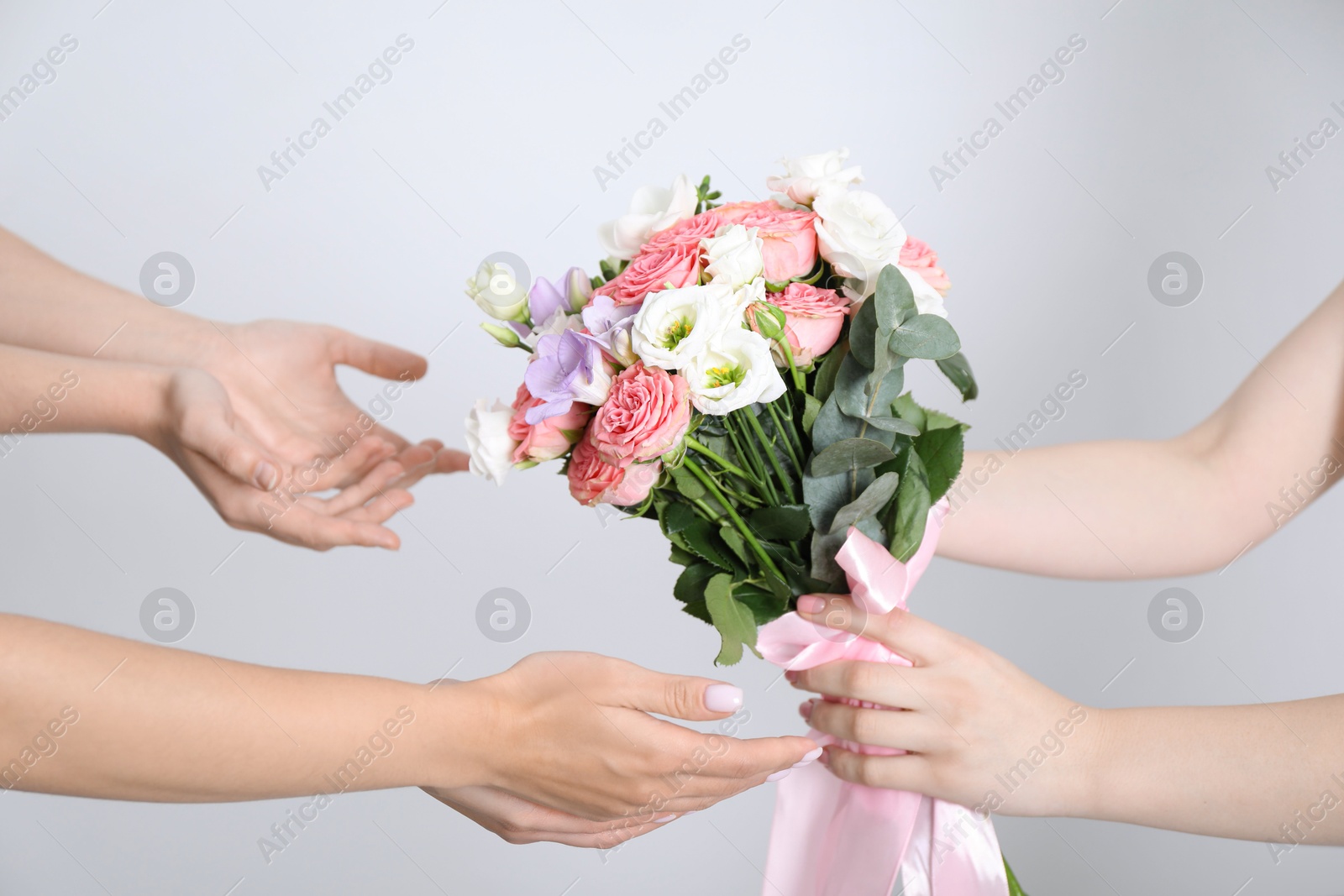 Photo of Bridesmaids giving beautiful wedding bouquet to bride on light background, closeup