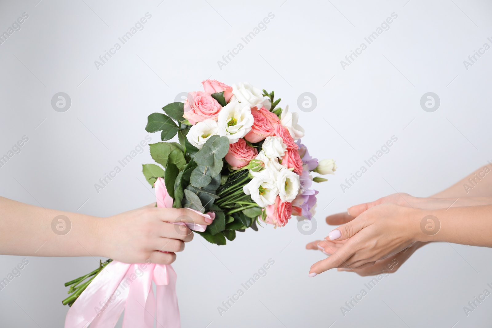 Photo of Bridesmaids giving beautiful wedding bouquet to bride on light background, closeup