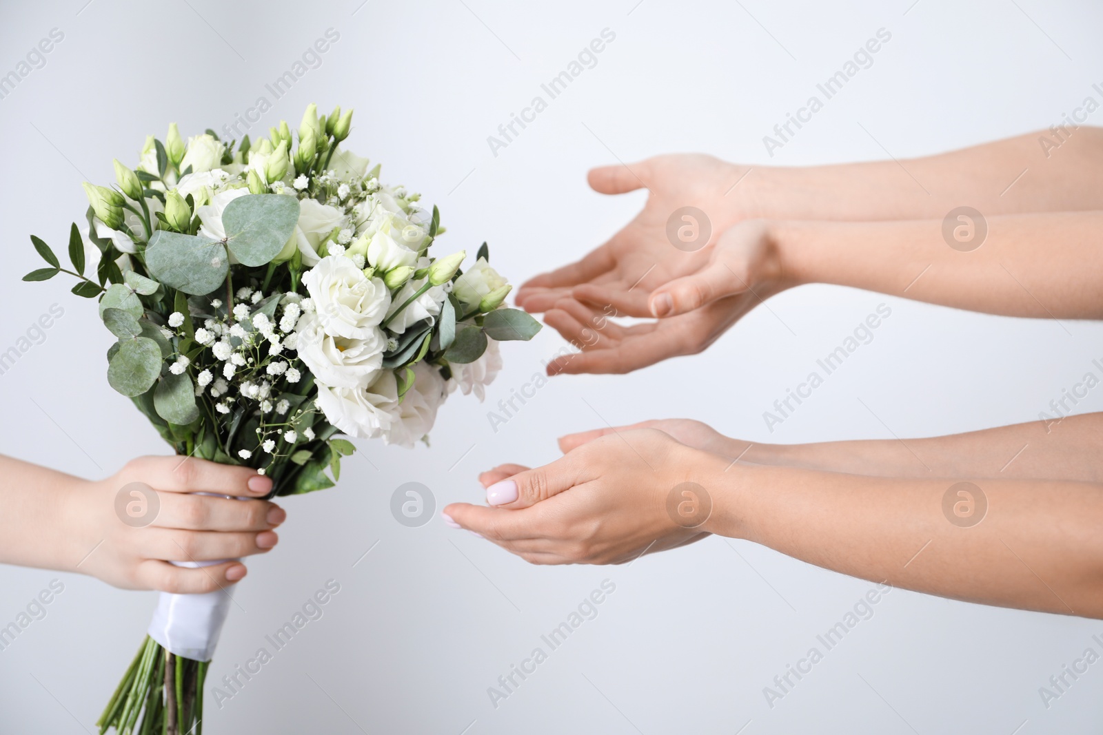 Photo of Bridesmaids giving beautiful wedding bouquet to bride on light background, closeup