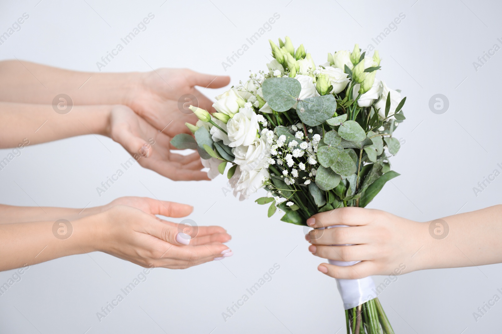 Photo of Bridesmaids giving beautiful wedding bouquet to bride on light background, closeup