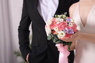 Photo of Bride with beautiful wedding bouquet and groom indoors, closeup