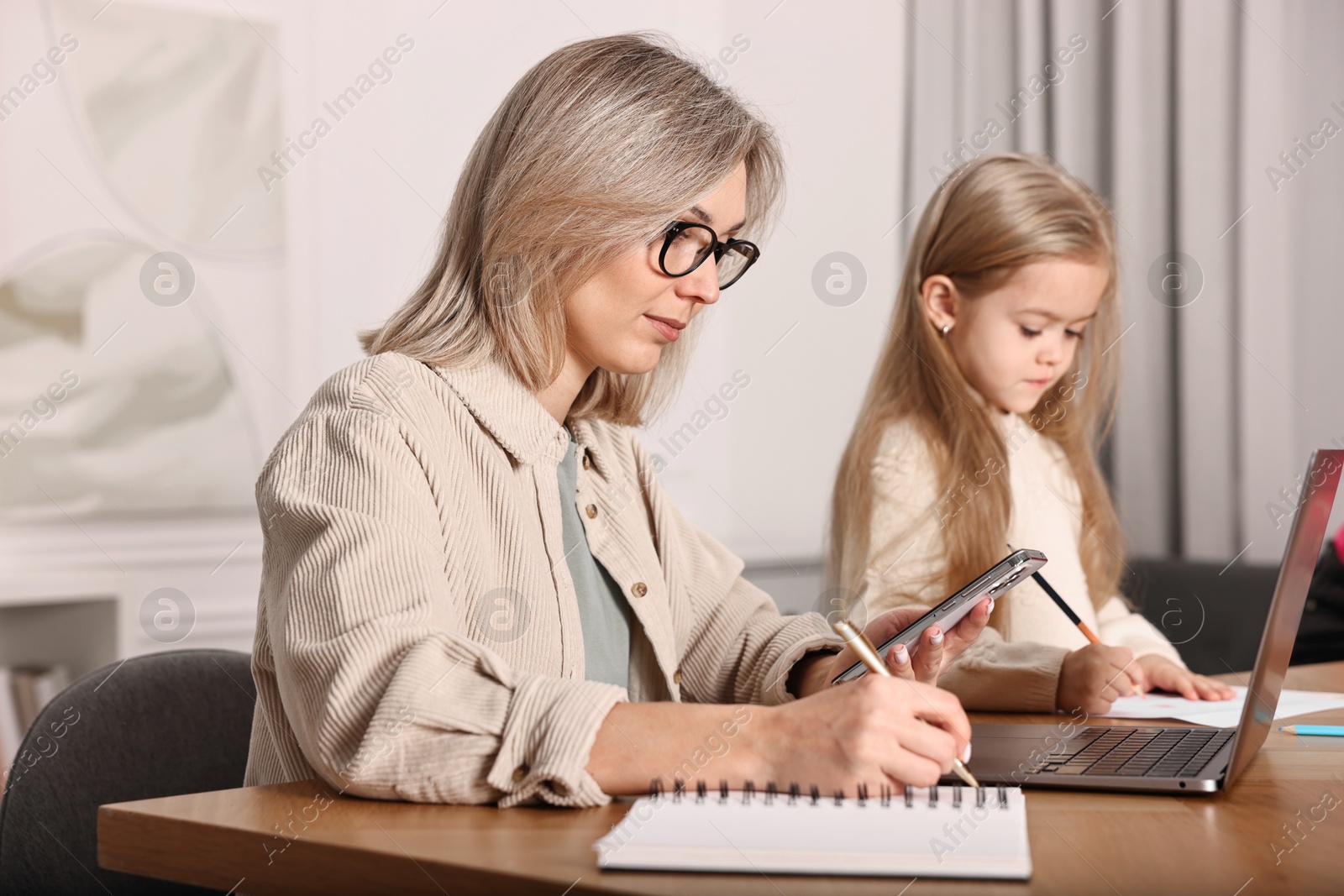 Photo of Single mother working and her daughter drawing at wooden table indoors