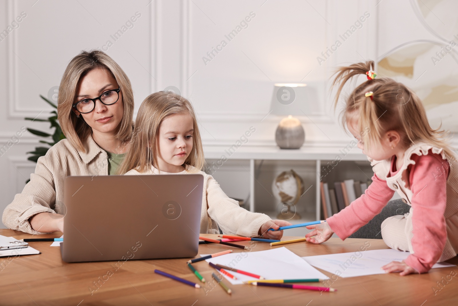 Photo of Single mother working and her children drawing at wooden table indoors