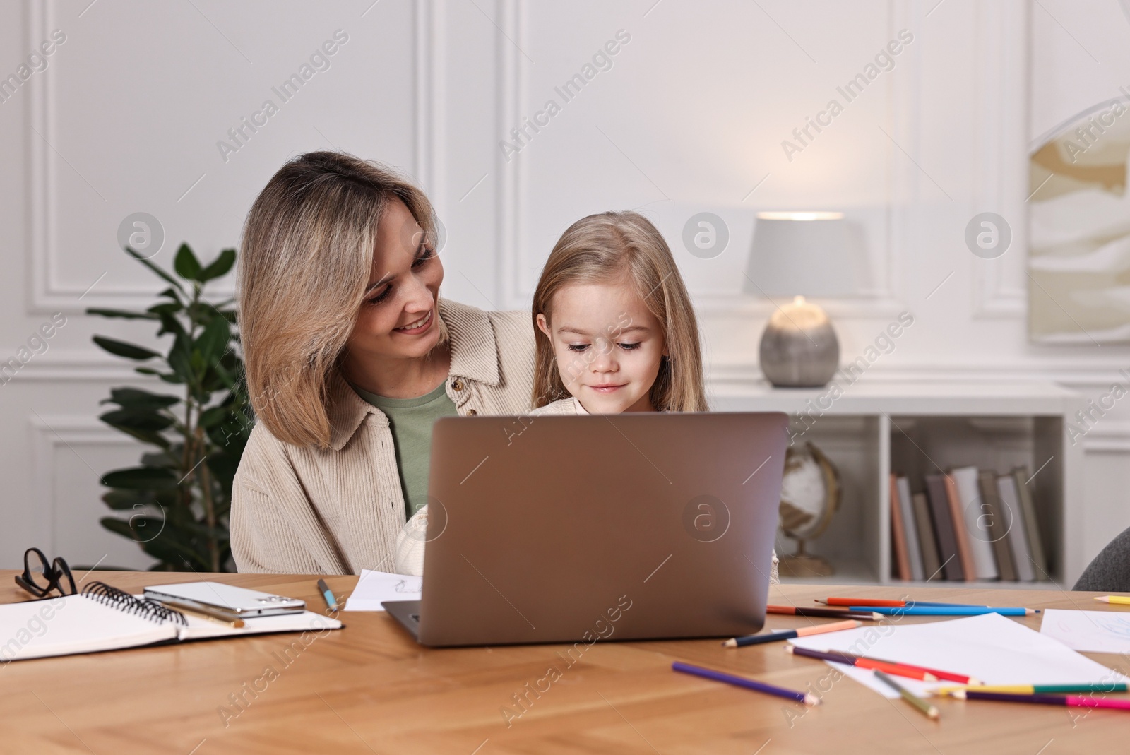 Photo of Work-family balance. Single mother with her daughter at wooden table indoors