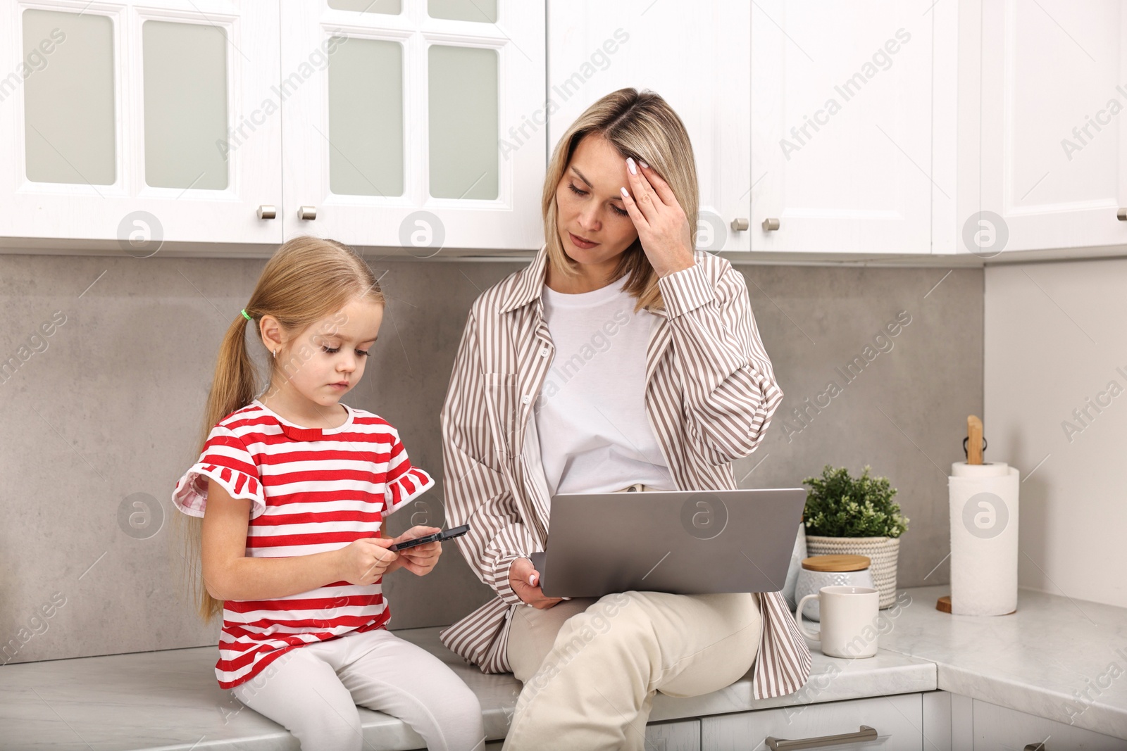 Photo of Single mother working with laptop and her daughter in kitchen