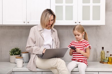 Photo of Work at home. Single mother talking by smartphone and her daughter in kitchen