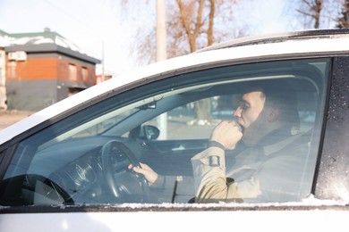 Photo of Sleepy driver yawning in his modern car, view from outside