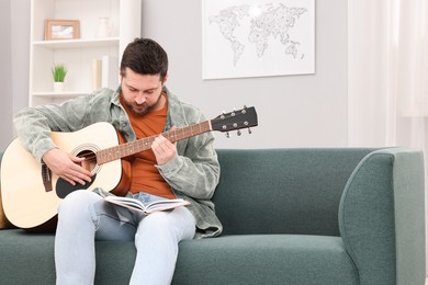 Photo of Relaxing hobby. Man with guitar and book on sofa at home