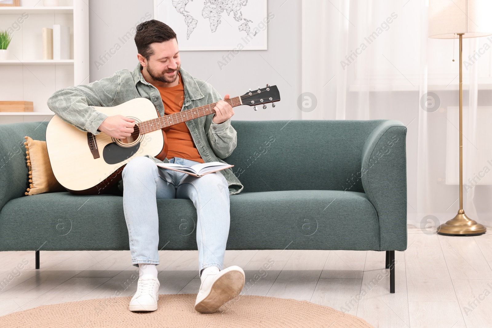 Photo of Relaxing hobby. Man with guitar and book on sofa at home