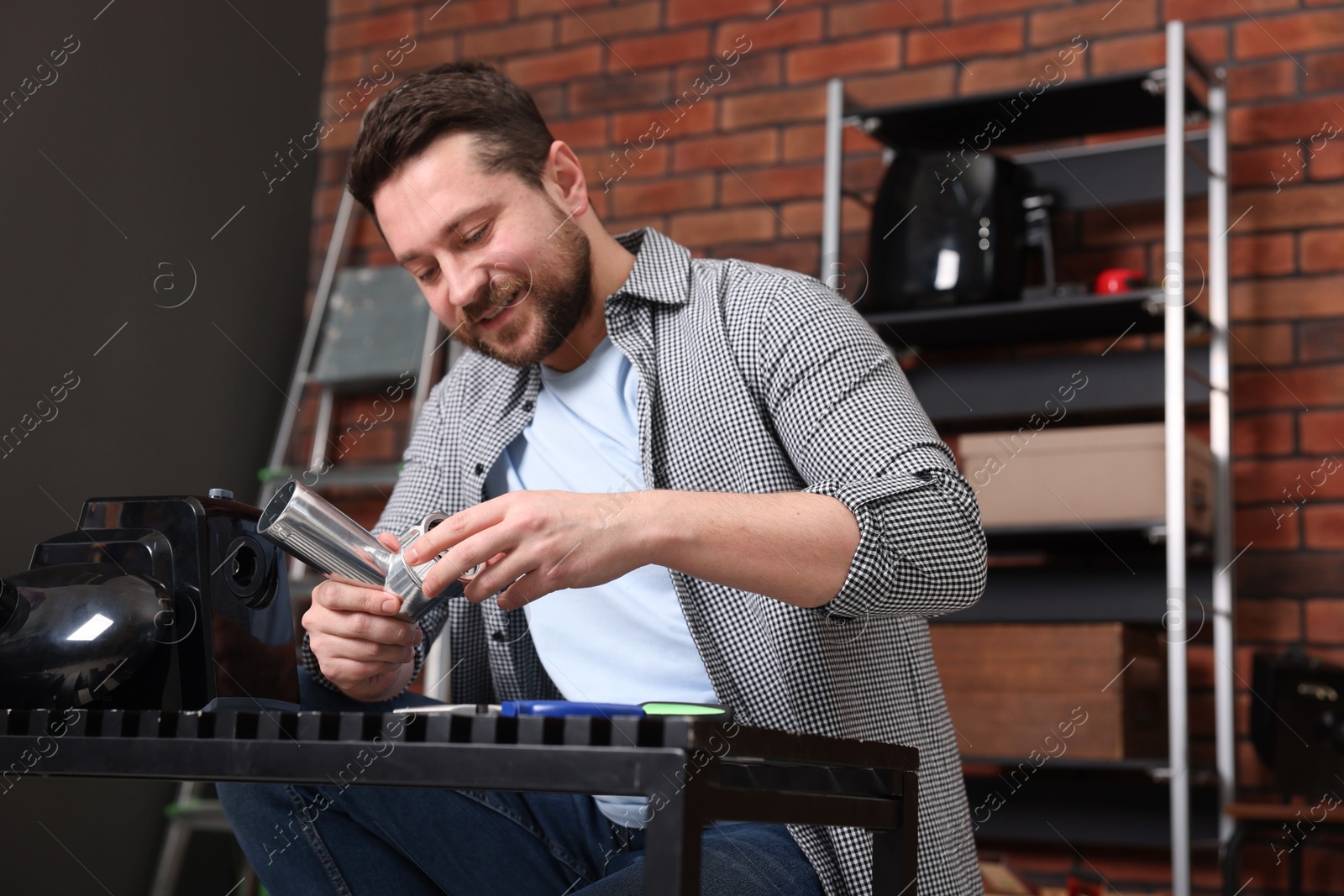 Photo of Relaxing hobby. Smiling man repairing electric meat grinder in workshop