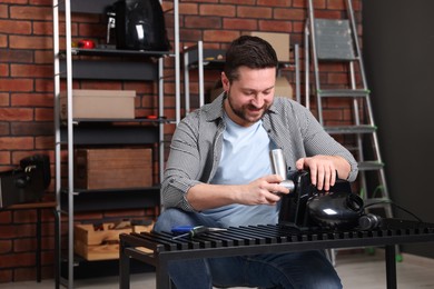 Photo of Relaxing hobby. Smiling man repairing electric meat grinder in workshop