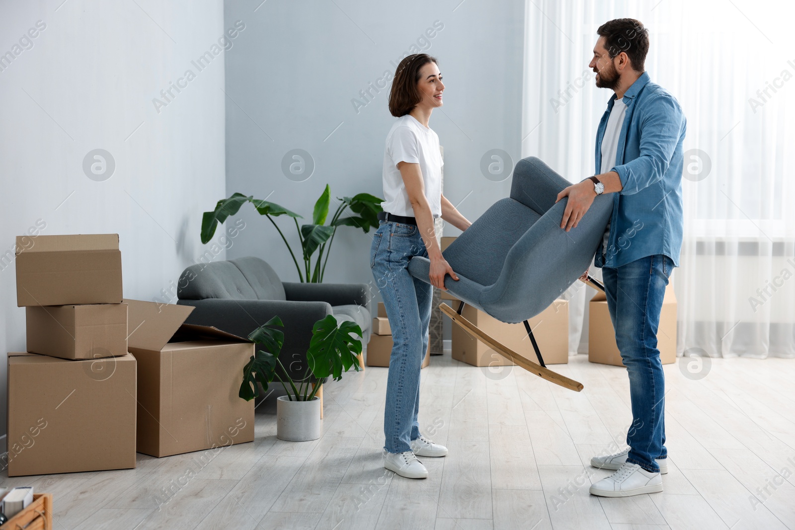 Photo of Moving day. Happy couple carrying chair in their new home