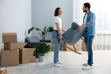 Photo of Moving day. Happy couple carrying chair in their new home