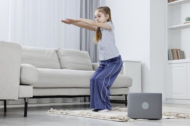 Photo of Little girl exercising near laptop at home, low angle view. Morning routine