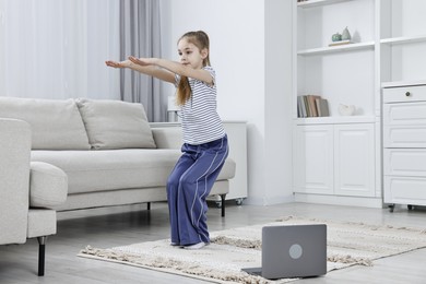 Photo of Little girl exercising near laptop at home. Morning routine