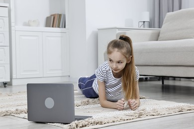 Photo of Little girl doing plank exercise near laptop at home. Morning routine