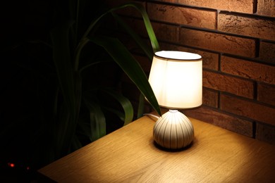 Photo of Glowing lamp on wooden table indoors, space for text