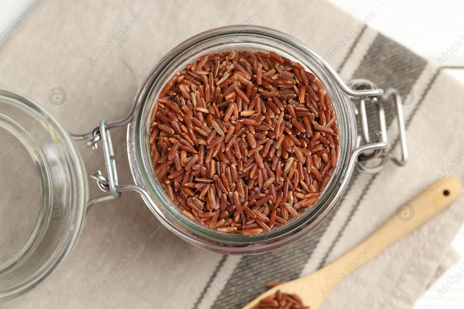 Photo of Raw brown rice in open jar and spoon on white table, top view