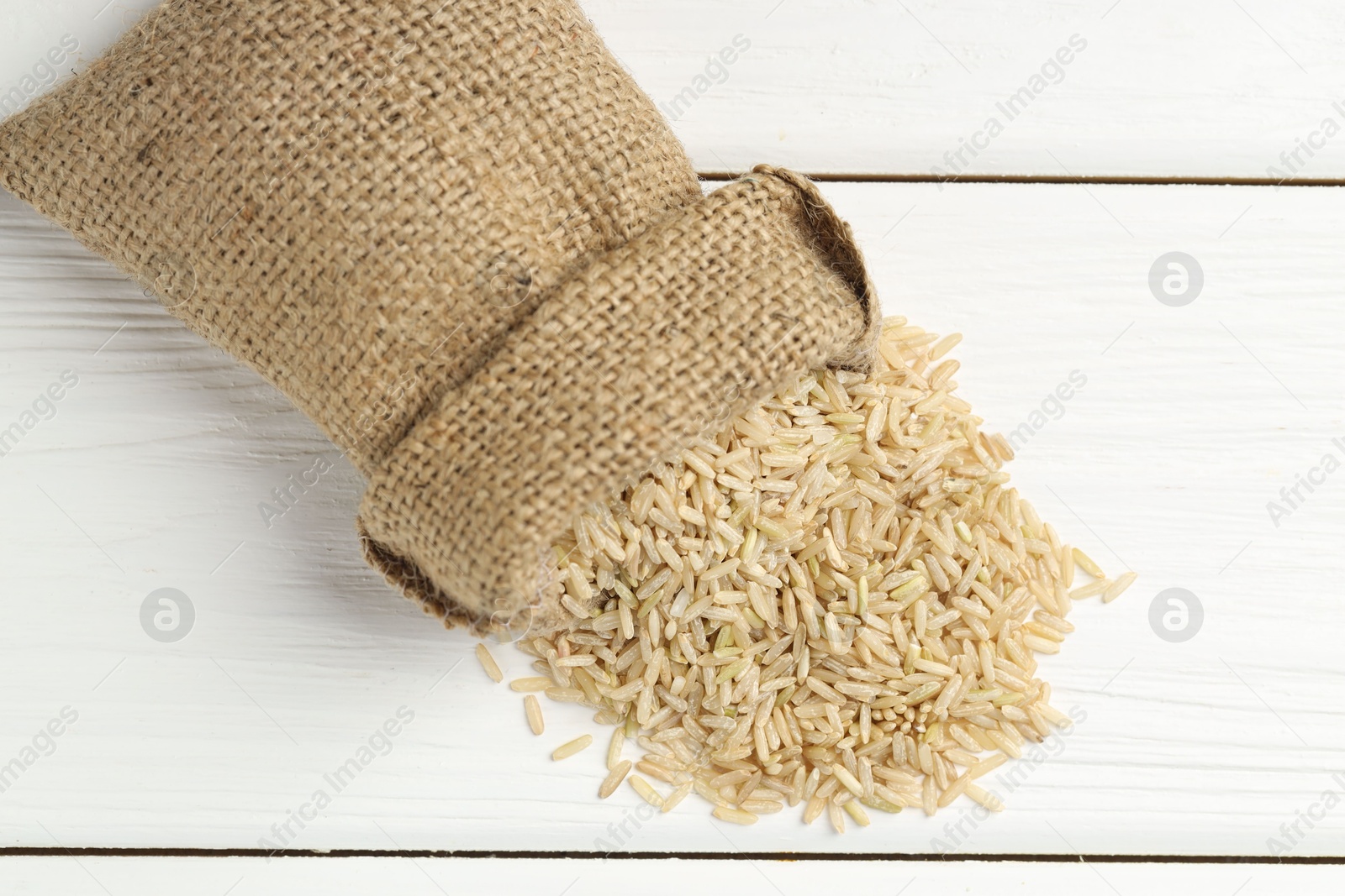 Photo of Raw brown rice in sack on white wooden table, top view