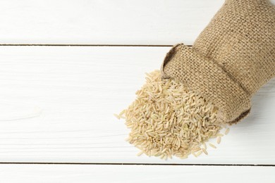 Photo of Raw brown rice in sack on white wooden table, top view. Space for text