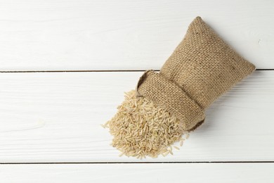 Photo of Raw brown rice in sack on white wooden table, top view. Space for text