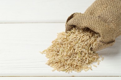 Photo of Raw brown rice in sack on white wooden table, closeup. Space for text