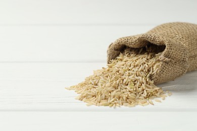 Photo of Raw brown rice in sack on white wooden table, closeup. Space for text