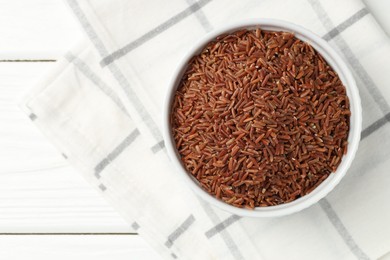 Photo of Raw brown rice in bowl on white wooden table, top view. Space for text