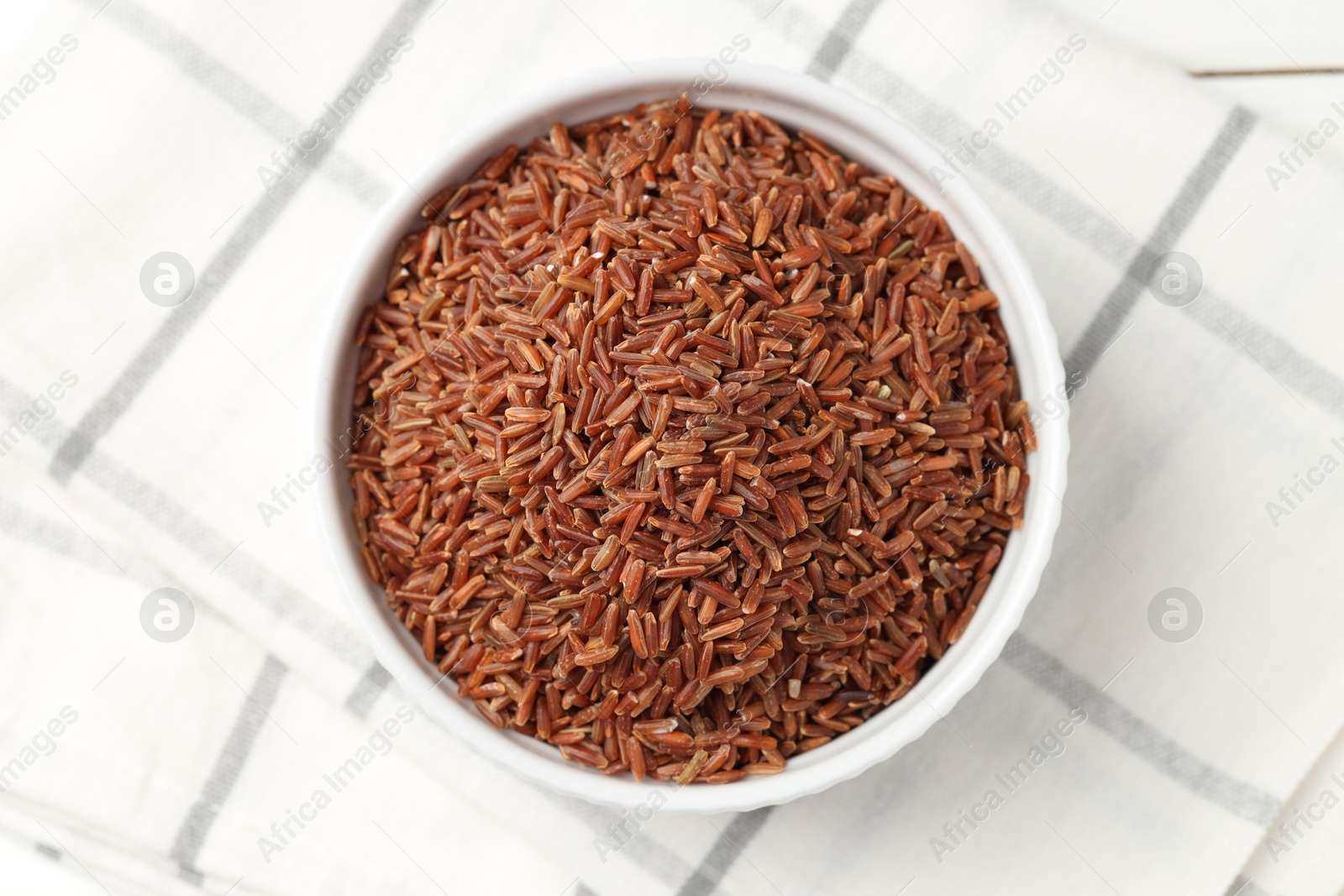 Photo of Raw brown rice in bowl on white table, top view