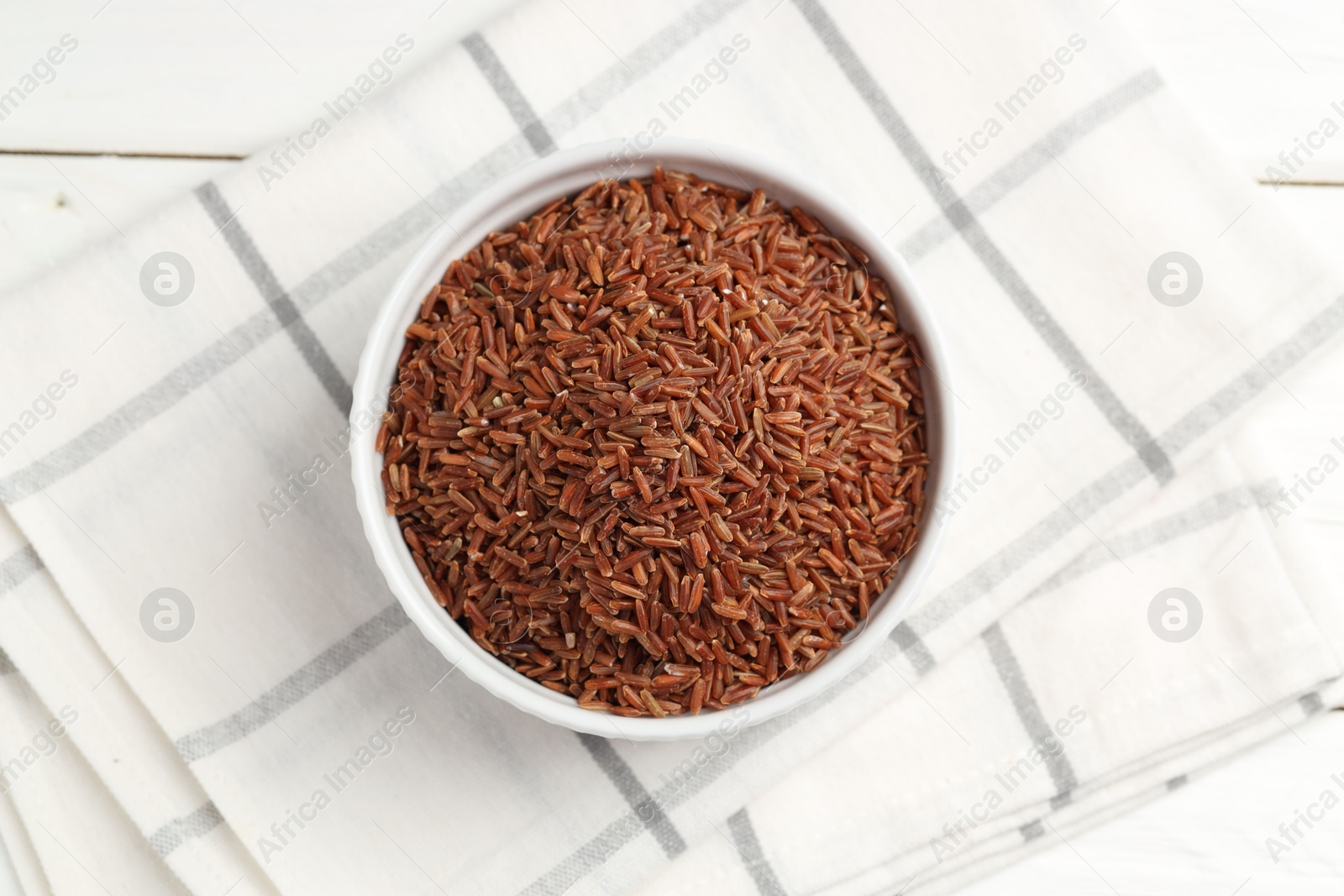 Photo of Raw brown rice in bowl on white wooden table, top view