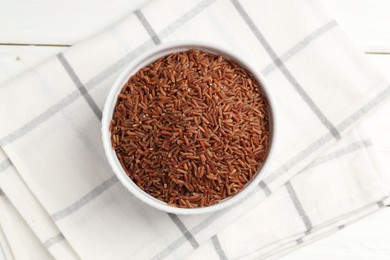 Photo of Raw brown rice in bowl on white wooden table, top view