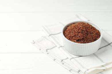 Photo of Raw brown rice in bowl on white wooden table, closeup. Space for text