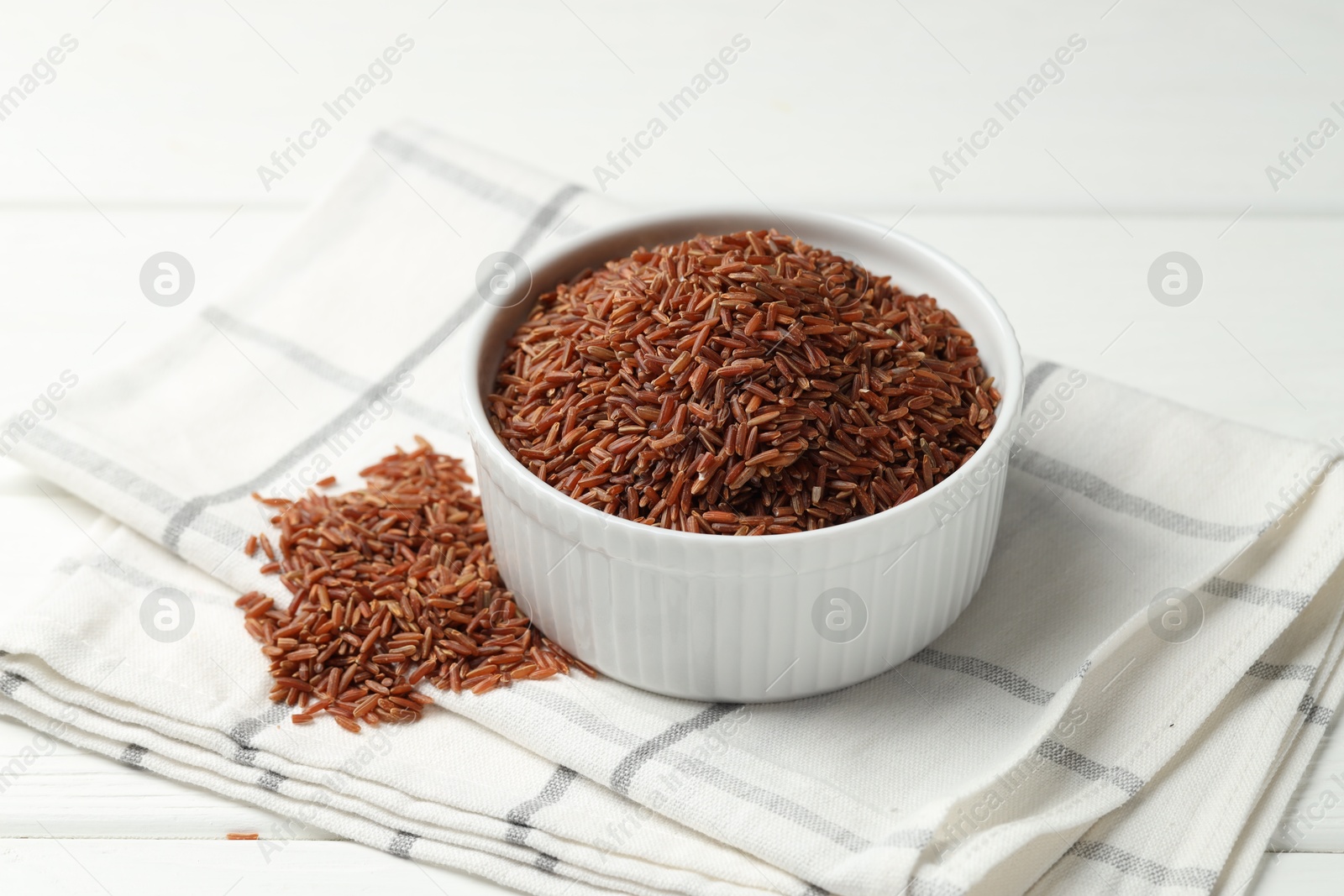 Photo of Raw brown rice in bowl on white wooden table, closeup