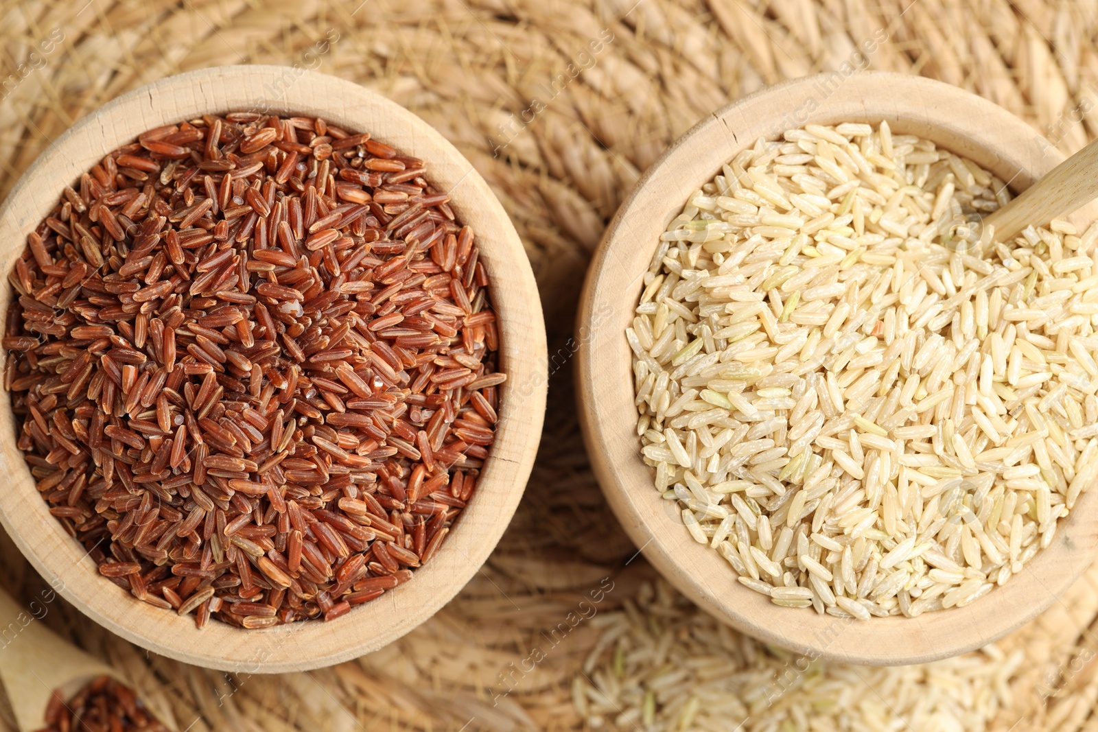 Photo of Different sorts of raw brown rice on wicker mat, top view