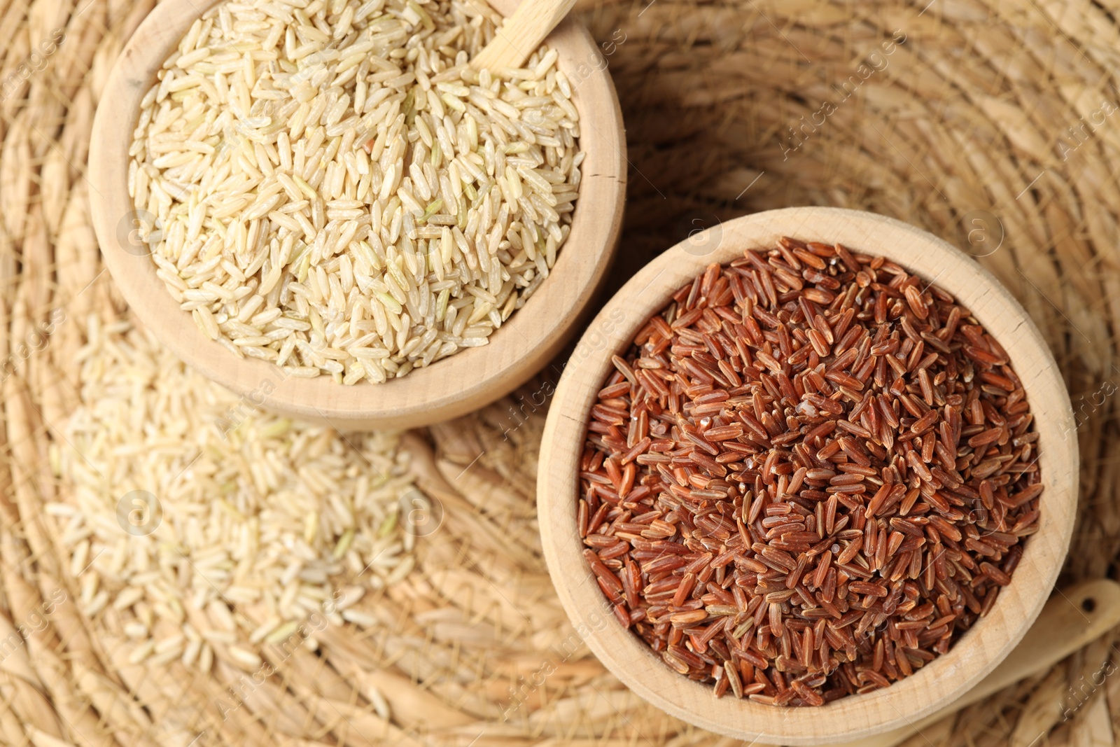 Photo of Different sorts of raw brown rice on wicker mat, top view