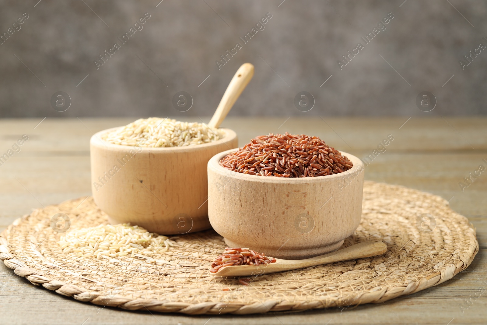 Photo of Different sorts of raw brown rice on wooden table against grey background, closeup.