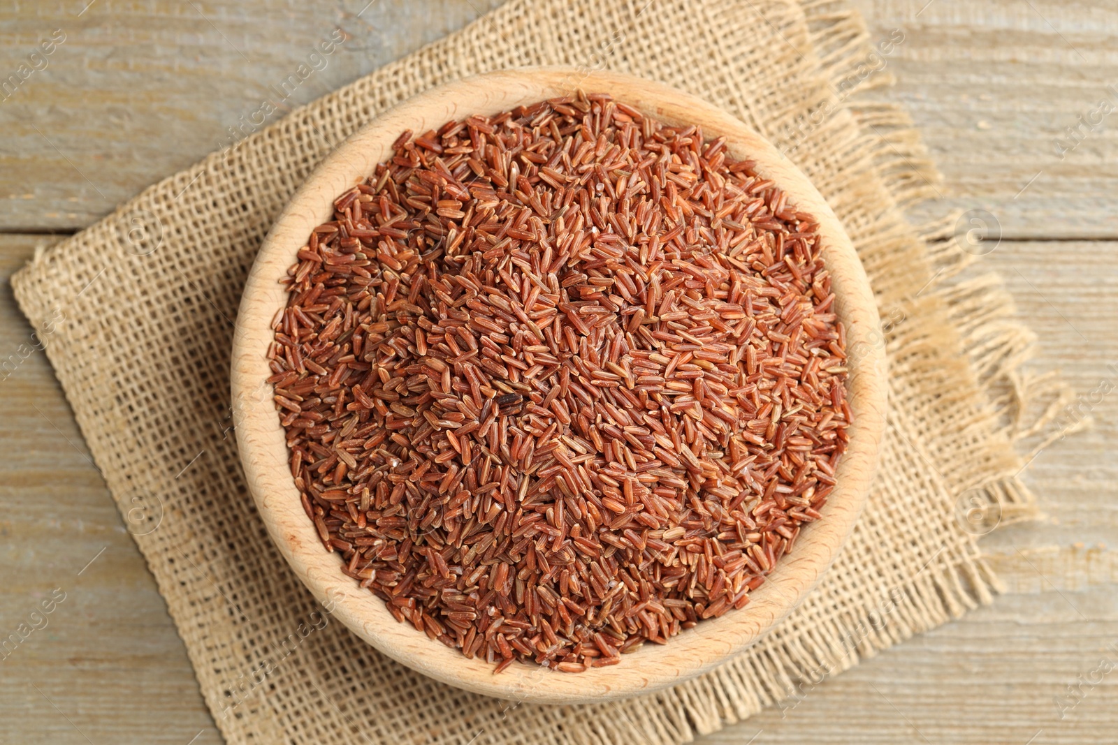 Photo of Raw brown rice in bowl on wooden table, top view