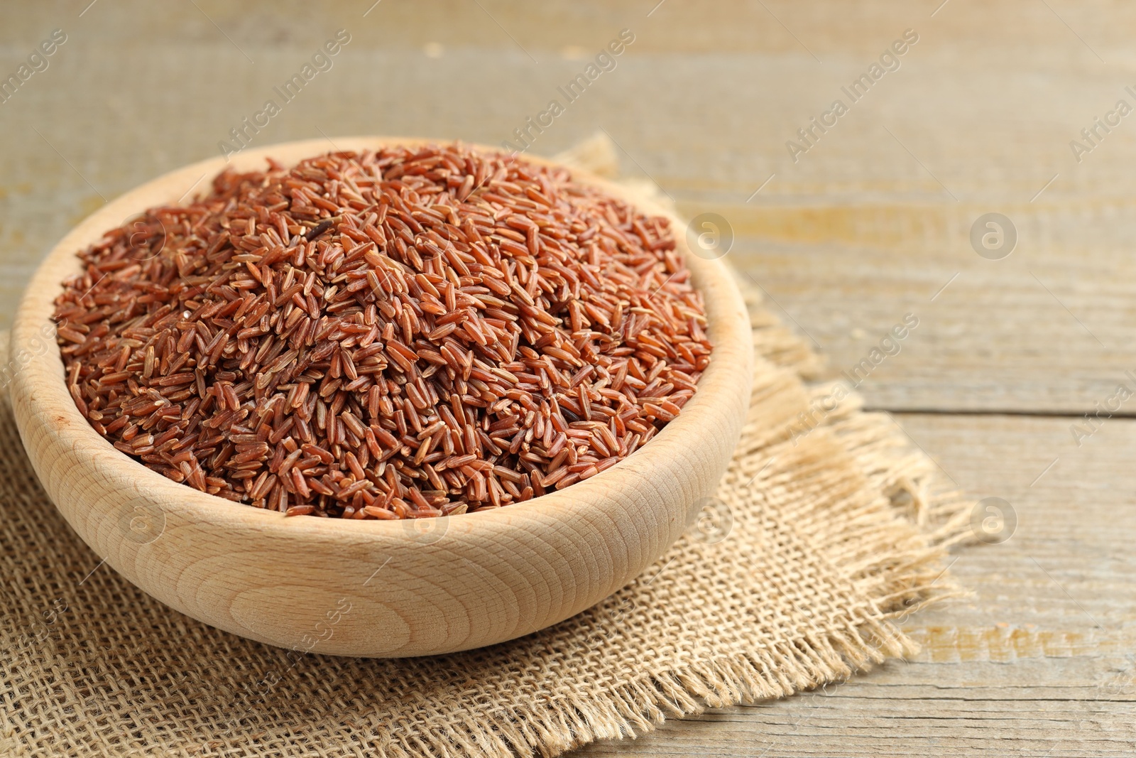 Photo of Raw brown rice in bowl on wooden table, closeup. Space for text