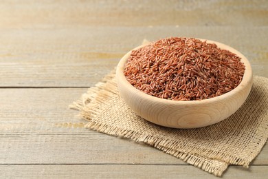 Photo of Raw brown rice in bowl on wooden table, closeup. Space for text