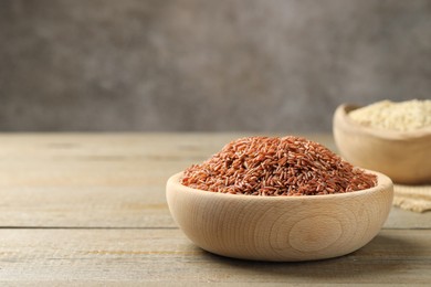 Photo of Raw brown rice in bowl on wooden table against grey background, closeup. Space for text