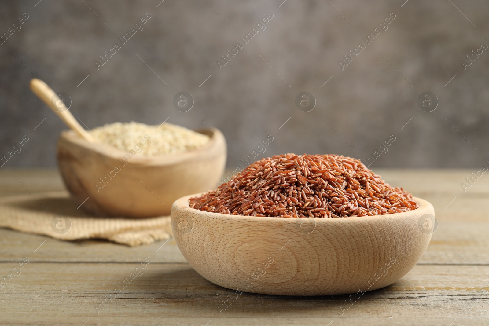 Photo of Raw brown rice in bowl on wooden table against grey background, closeup