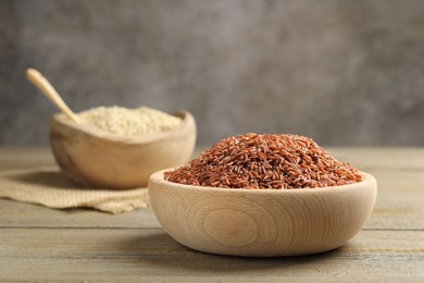 Photo of Raw brown rice in bowl on wooden table against grey background, closeup