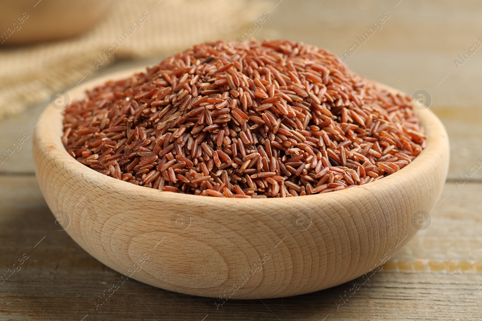 Photo of Raw brown rice in bowl on wooden table, closeup