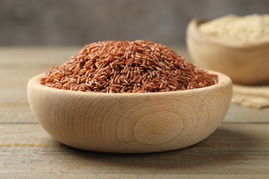 Photo of Raw brown rice in bowl on wooden table against grey background, closeup